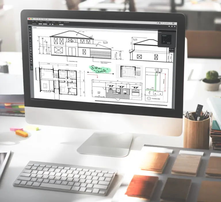 Desktop computer showing house elevations and floor plans in drafting software, on a desk with material samples
