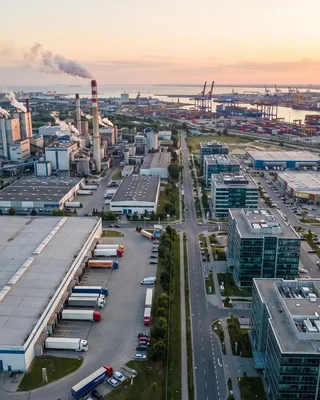 Aerial view of a commercial district at dusk with glass office towers, retail units, distribution warehouses and a container port beyond