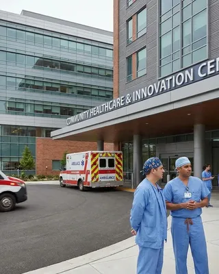 Clinical staff outside a healthcare and innovation centre, with the ambulance canopy, curtain wall and metal panel facade behind